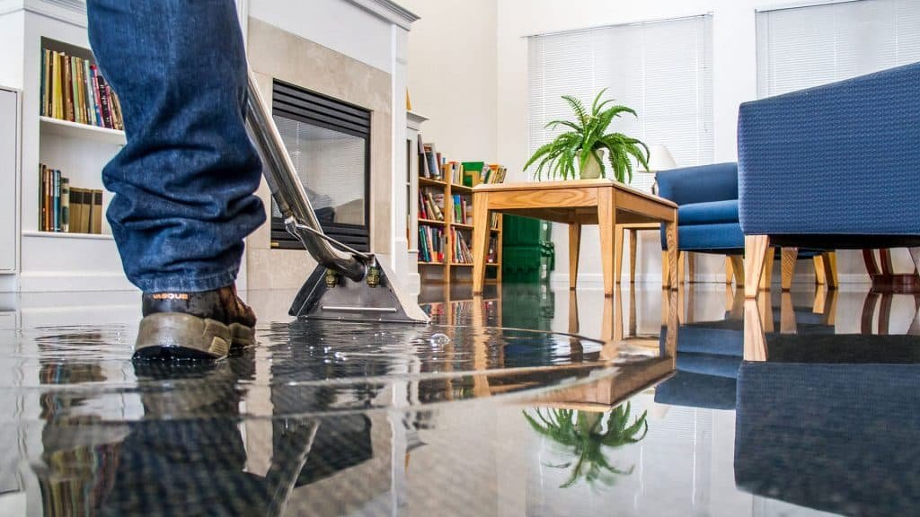 Technician extracting standing water from a hardwood floor in a living room